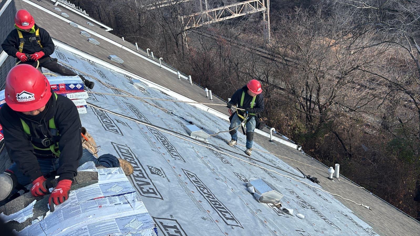 Adilay Roofing crew with safety harnesses and hard hats installing underlayment on a steep roof